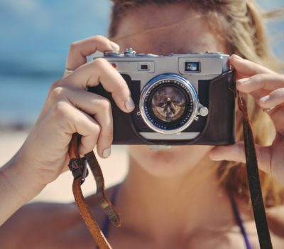 Young woman at the beach whose face is obscured by a vintage camera