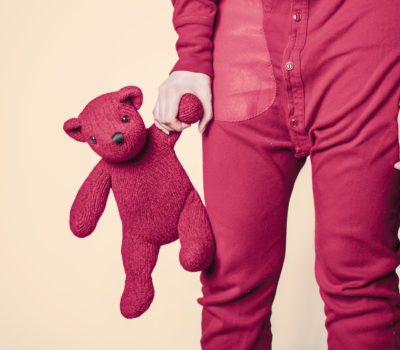 A person in a pair of red pajamas holds a red teddy bear by its paw