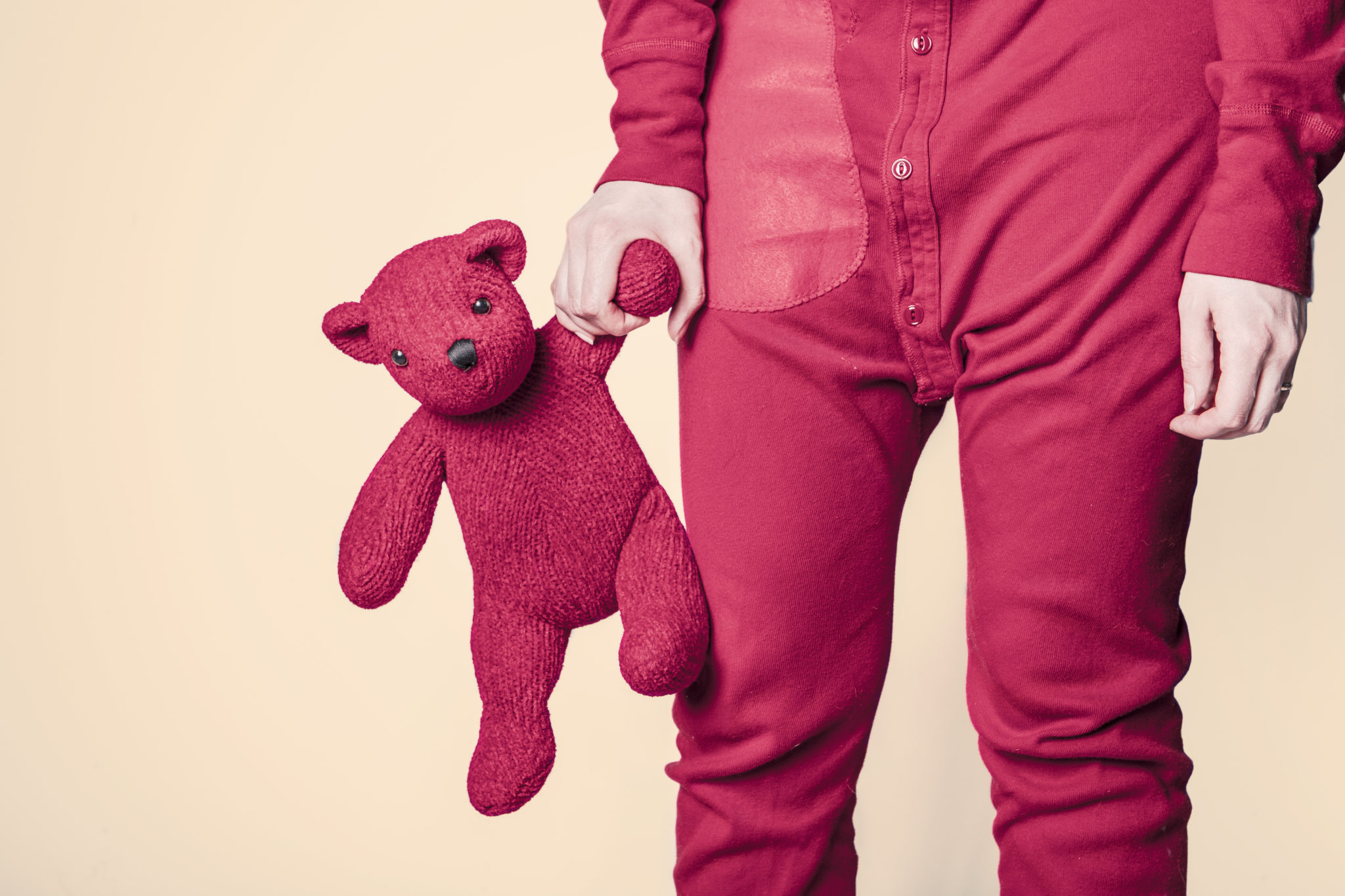 A person in a pair of red pajamas holds a red teddy bear by its paw